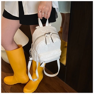 Detail of a white mini backpack featuring crocodile texture and metallic zippers