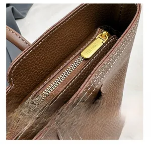 Detail of smooth gold zipper on dark brown lychee leather tote with white stitching