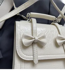 Detail of cream pleated leather bag with a bow accent and a slender shoulder strap