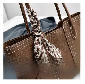 Close-up of brown leather tote bag handle with geometric scarf and white contrast stitching