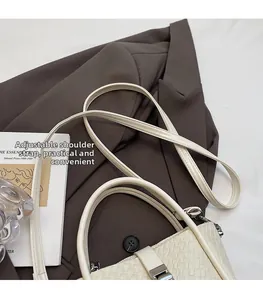 Détail du sac seau tressé crème avec bandoulière réglable sur un blazer chic