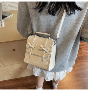 Close-up of cream textured PU leather crossbody bag featuring dual bow accents and handle