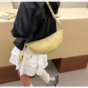 Detail of yellow crescent bag with knotted strap and colorful bird charm on leather