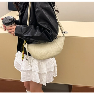 Detail of beige croissant crossbody bag with pebble leather texture and knotted shoulder strap