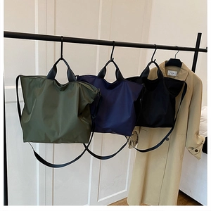 Three large nylon tote bags in olive, navy, and black colors hanging on a rack
