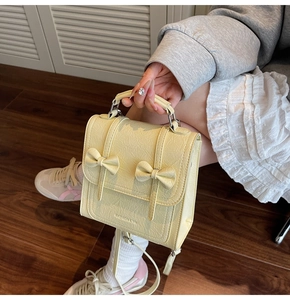 Detail of cream mini backpack featuring crinkled leather texture and decorative bows