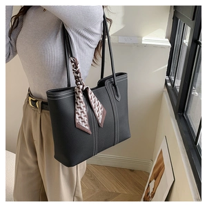 Detail of black pebbled leather tote bag with white stitching and geometric silk scarf