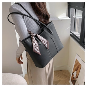 Detail of black pebbled leather tote bag with white stitching and floral silk scarf accessory