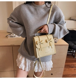 Detail of cream glossy PU shoulder bag featuring dual bow design and brand lettering