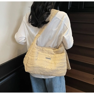 Detail of a large beige quilted tote bag with wave stitching and a metal logo plaque
