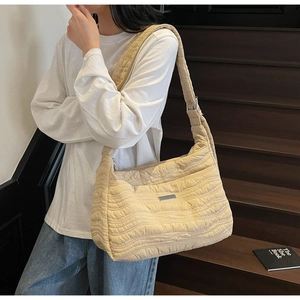 Detail of beige quilted wave tote bag with adjustable wide strap and metallic logo plate
