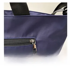 Macro detail of high-density navy nylon tote with a smooth silver metal zipper and black strap