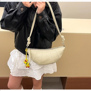Detail of creamy croissant bag with textured leather, vertical stitching and duck charm