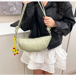 Detail of light green pebbled leather croissant bag with woven strap and yellow duck charm