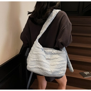Detail of light blue quilted shoulder bag with wave texture and wide strap on model