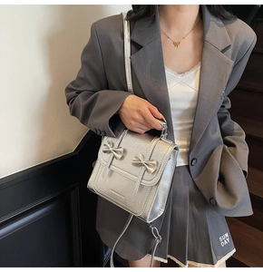 Silver shoulder bag with metallic crinkled texture and dual 3D bow accents worn by model