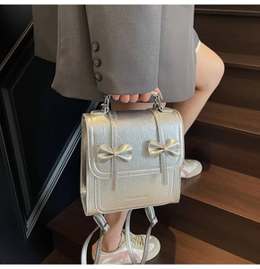 Close-up of silver textured backpack with 3D bow detail held by a model on stairs