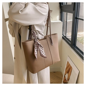 Detail of brown litchi leather tote bag with white stitching and floral silk scarf charm