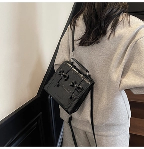 Rear view of model carrying black patent leather handbag with dual bow accents and strap