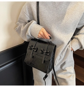 Detail of glossy black crinkled leather mini bag featuring cute bow accents and metal buckle