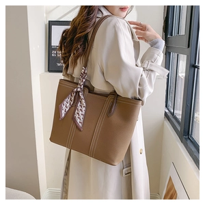Close-up of brown pebbled leather tote bag with white stitching and patterned silk scarf