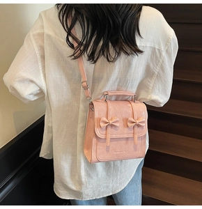 Detailed view of pink glossy crossbody bag with two bows and adjustable shoulder strap
