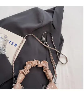 Close-up of pleated handle and metal ball adjustment on a beige leather handbag