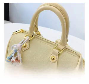 Detail of cream lychee leather boston bag with golden hardware and decorative charm