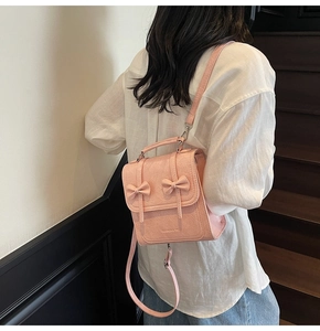 Pink faux leather backpack with bow accents shown on a model in a minimalist setting