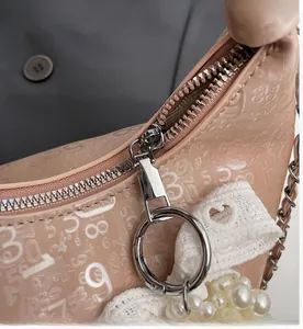 Detail of smooth metal zipper and pearl lace charms on a beige pleated handbag