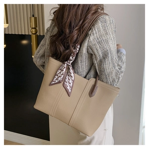 Detail of beige leather tote bag with lychee grain and decorative silk scarf on handle