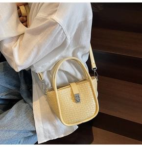 Beige woven leather bucket bag shown on a model against a wooden staircase background