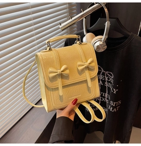 Detail of light yellow patent leather backpack featuring decorative bows and handle