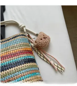 Detailed close-up of colorful striped straw bucket bag with white handle and bear charm