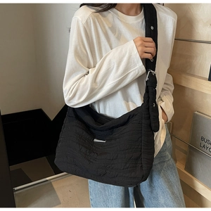 Detail of black quilted shoulder bag with wide strap and silver metal logo plate