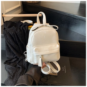 Detail shot of mini cream faux-snakeskin backpack with a bow-zipper pull and top handle