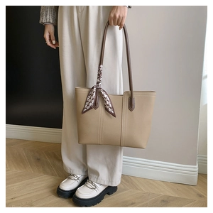Detail of beige lychee grain leather tote bag with stylish silk scarf on handle for work
