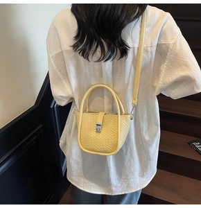 Close-up of bright yellow woven texture bucket bag with crossbody strap and silver hardware