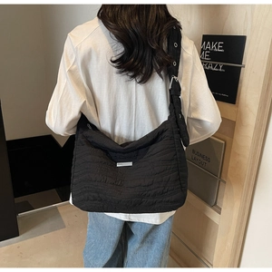 Detail of black quilted shoulder bag featuring wave texture and adjustable wide strap