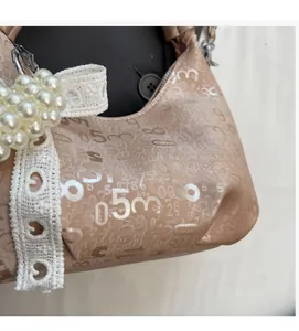 Close-up of beige shoulder bag featuring pearl handle, lace ribbon, and digital print