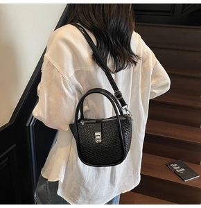 Detail of black woven texture on bucket bag with silver metal lock and leather strap