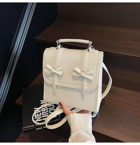 Detail of white textured PU leather backpack with decorative bows and metal clasp