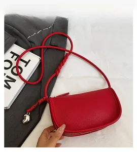 Détail du sac selle rouge en cuir grainé avec pendentif coeur argenté et bandoulière tressée