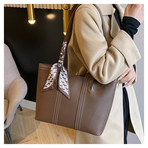 Detail of dark brown leather tote bag with white stitching and houndstooth scarf on handle