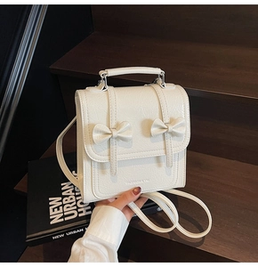 Detailed view of off-white PU leather backpack with decorative bows on wooden stairs
