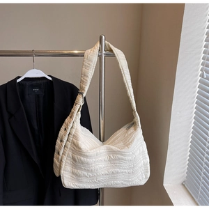 Close-up of beige quilted puffy shoulder bag with wave pattern and wide strap detail