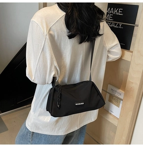 Détail du sac bandoulière en nylon noir avec cordon de zip et logo latéral en relief
