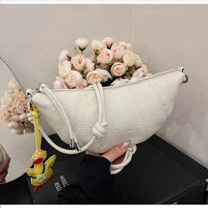 Detailed close-up of white croissant bag with pebble leather texture and duck charm