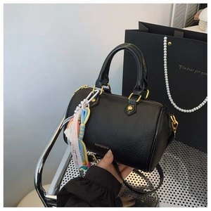Close-up of black pebble leather Boston bag with gold buckle and woven charm