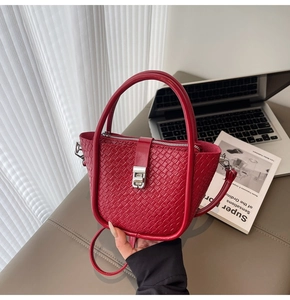 Detail of red woven bucket bag with circular handle and silver lock in a lifestyle setting